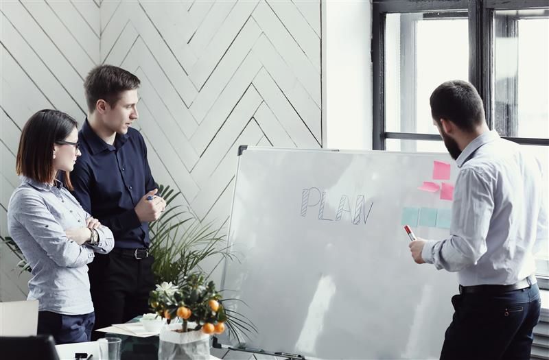 Three HR professionals discussing HR management strategies at a whiteboard in a modern office.